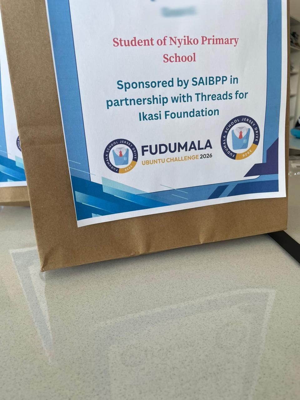 Close-up of a Fudumala Pack label: Student of Nyiko Primary School, Sponsored by SAIBPP in partnership with Threads for Ikasi Foundation, Fudumala Ubuntu Challenge 2026