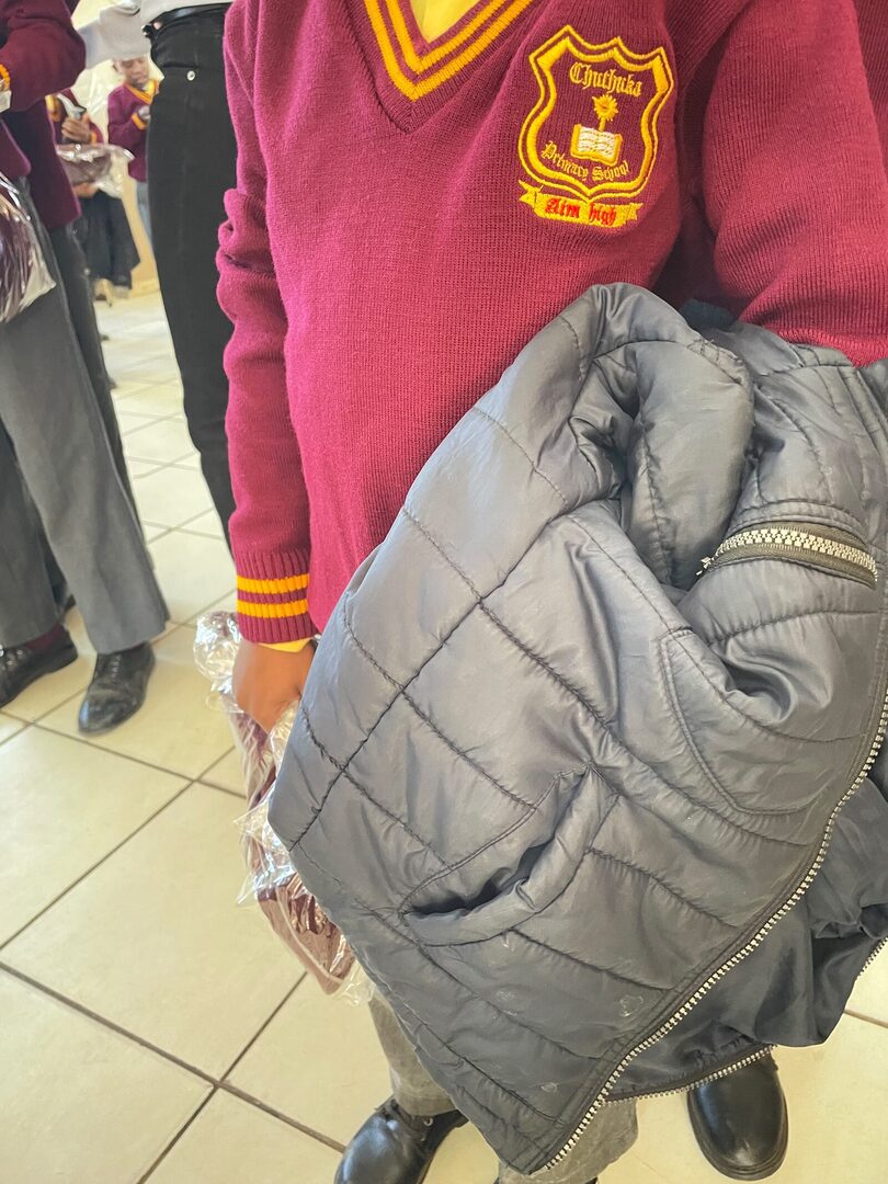 Close-up of the Thuthuka Primary School crest and Aim High motto embroidered on a maroon and gold ZS Uniforms school jersey