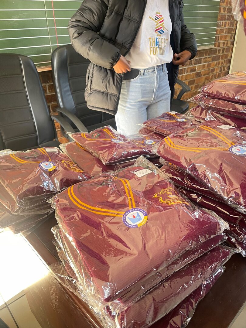 Stacks of sealed maroon Thuthuka Primary School jerseys supplied by ZS Uniforms, each carrying a learner name label, 30 July 2026